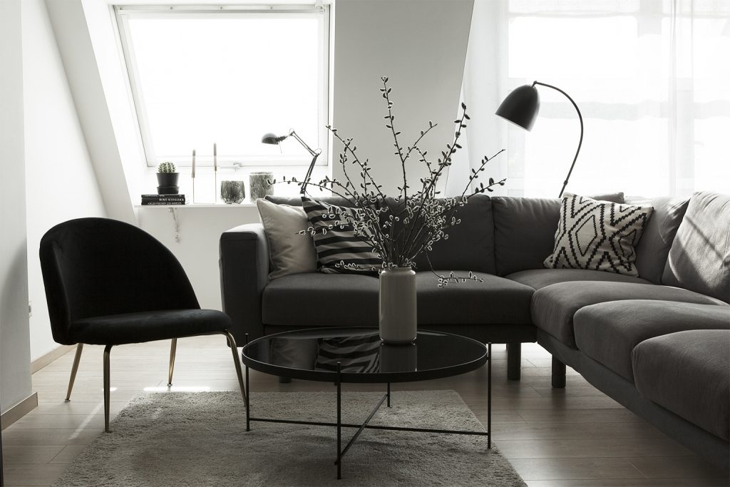 Monochromes Wohnzimmer mit grauer Couchlandschaft mit Kissen, schwarzem Loungesessel, schwarzem runden Tisch