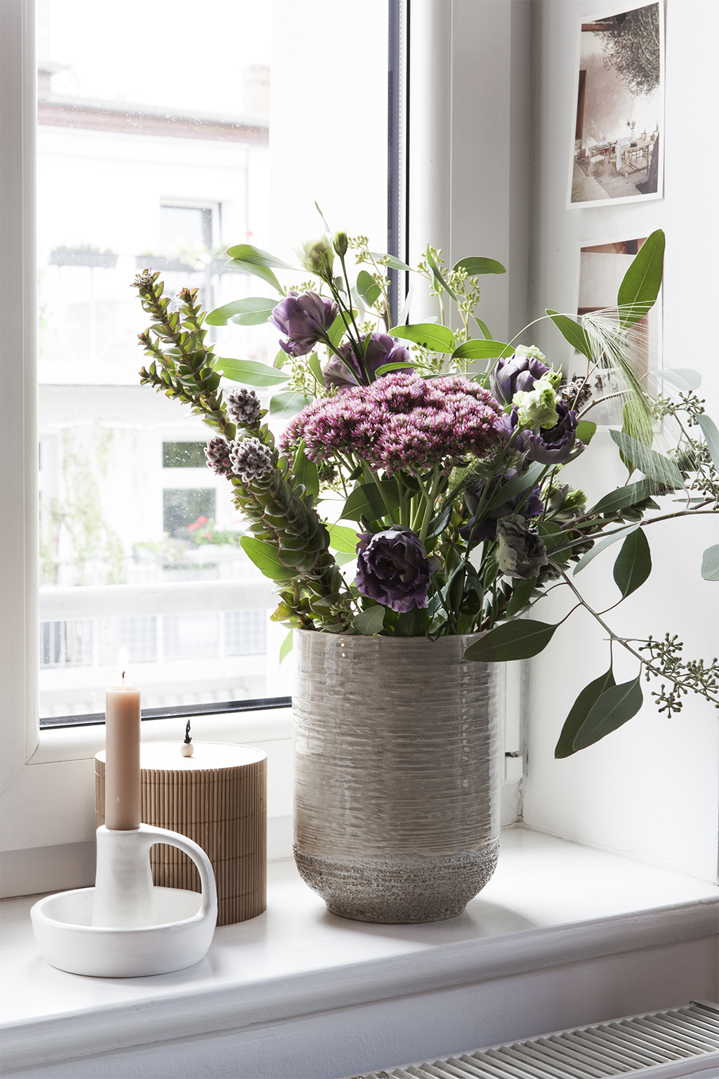 Blumenstrauß in Vase auf einem Fensterbrett mit Kerze und Holzdose