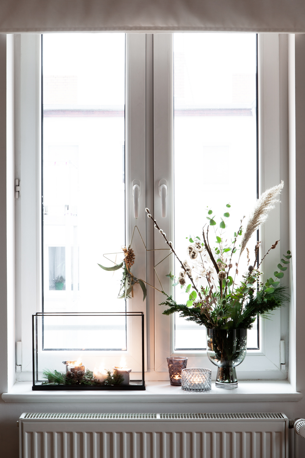 Blumenstrauß mit Glasvase und Teelichtern und Glasvitrine auf Fensterbank