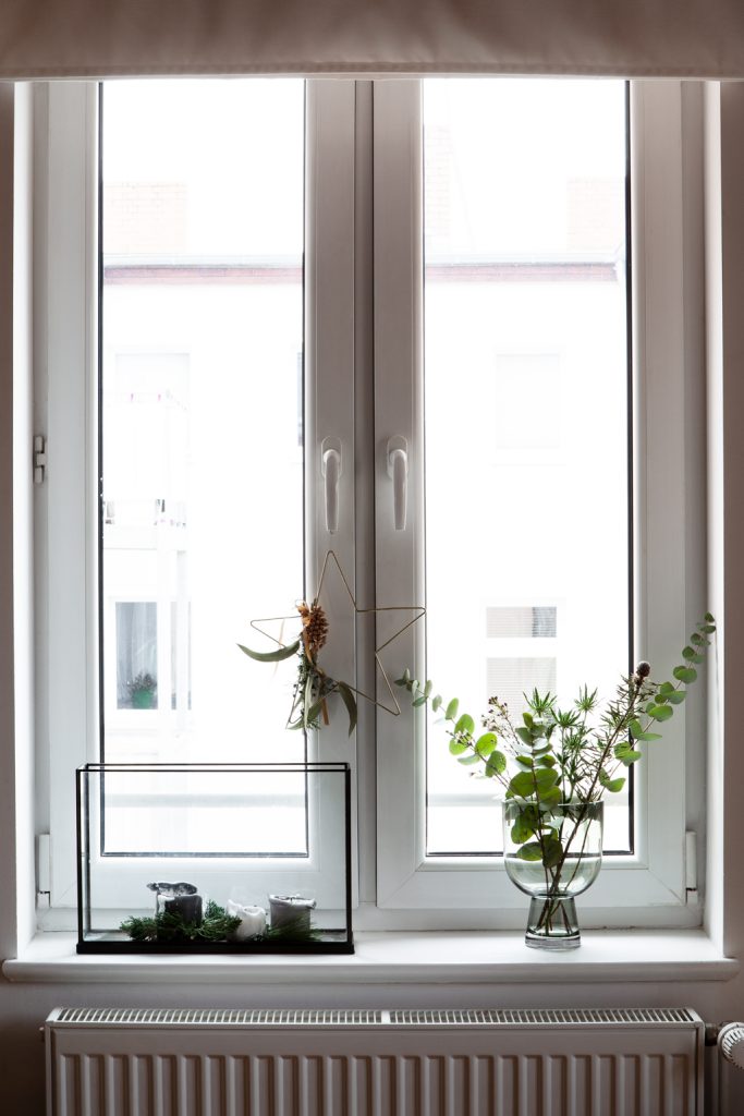 Einzelne Blumenstiele mit Glasvase und Teelichtern und Glasvitrine auf Fensterbank