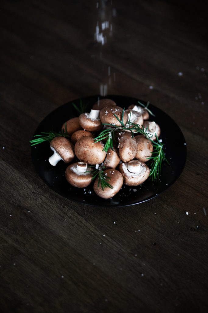 Pilze in schwarzer Keramikschale mit grobem Salzkörnern und Rosmarinzweigen