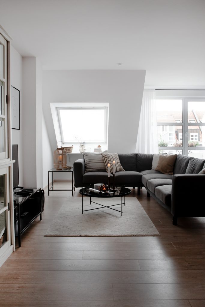 in warmen, erdigen Tönen eingerichtetes Wohnzimmer mit grauem Sofa, Wohnzimmertisch in Schwarz und hellen Teppich - von Hej.Hem Interior